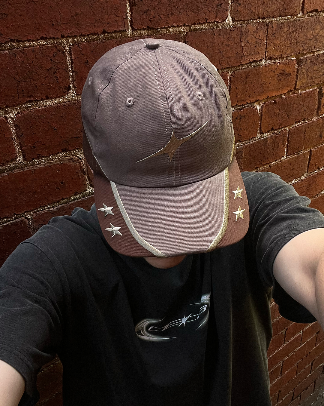 Person wearing a brown cap with star designs against a brick wall