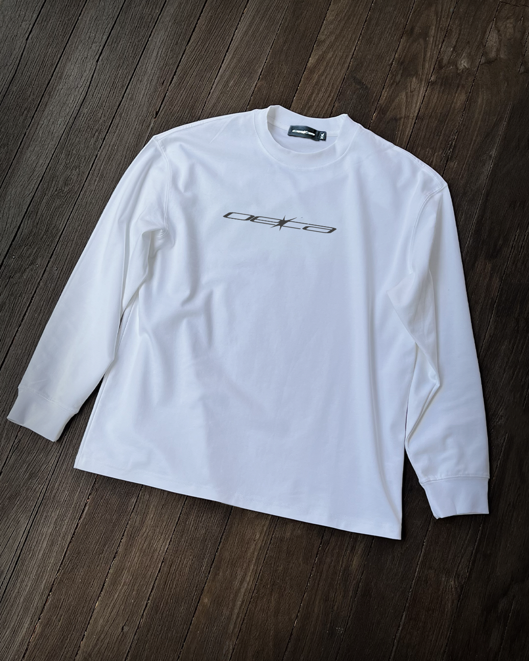 White long-sleeve shirt with a logo on a wooden surface