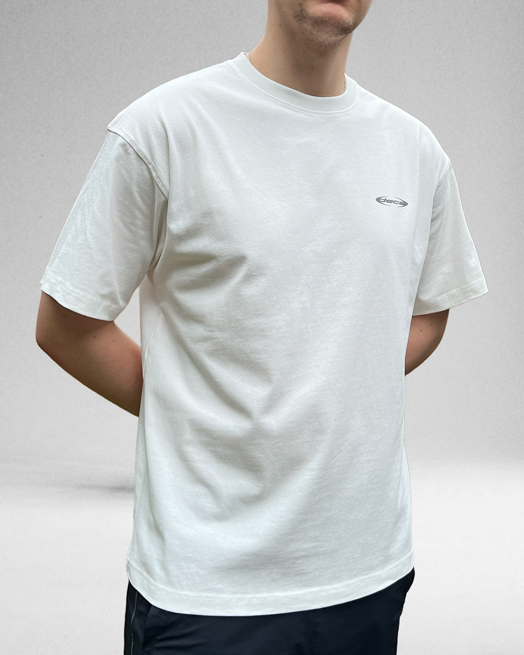 Person wearing a white t-shirt with a small logo on a plain background