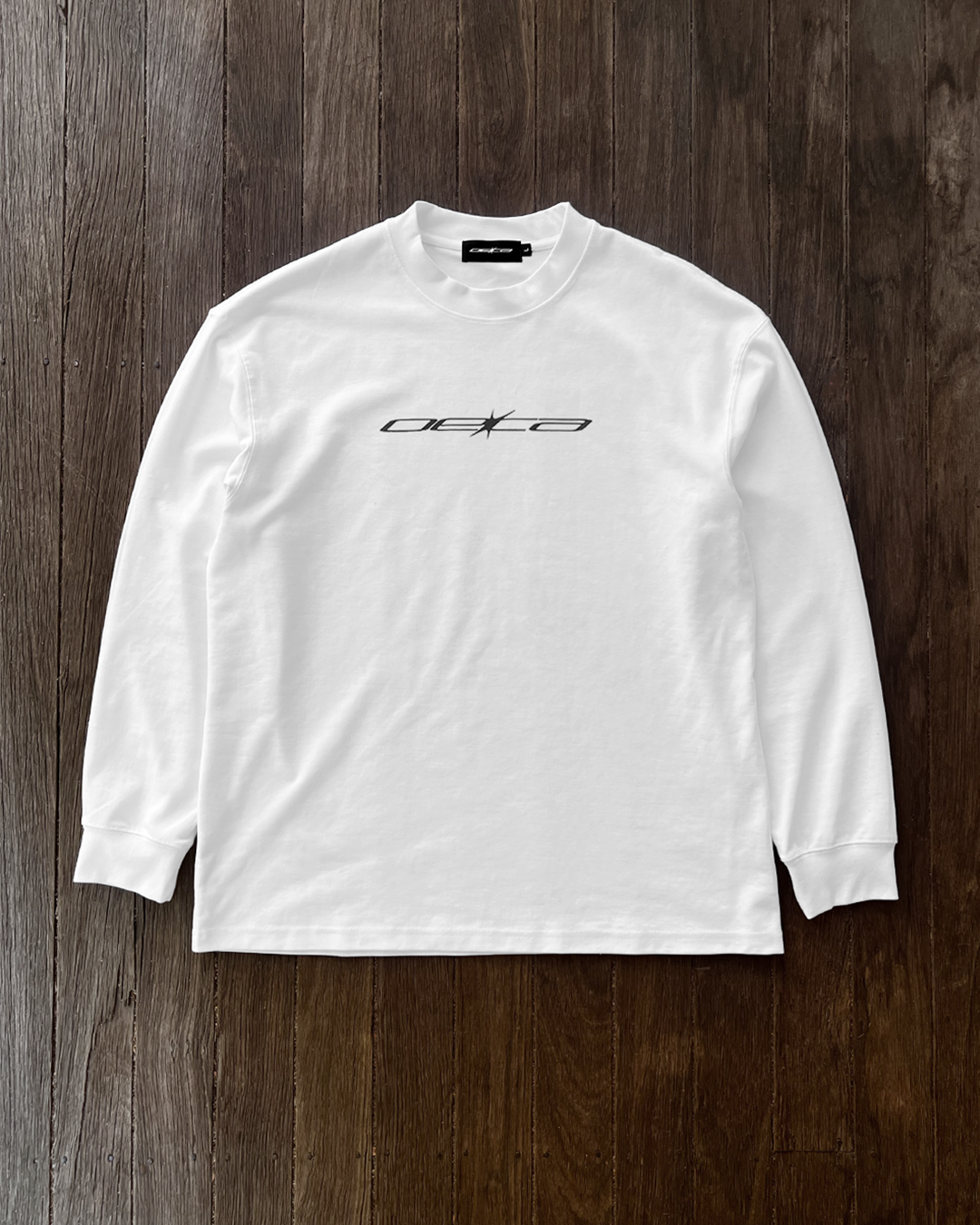 White long-sleeve shirt with a logo on a wooden surface