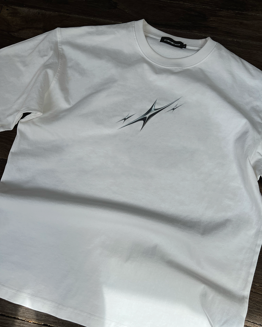 White t-shirt with a 3 silver stars graphic design on a wooden surface