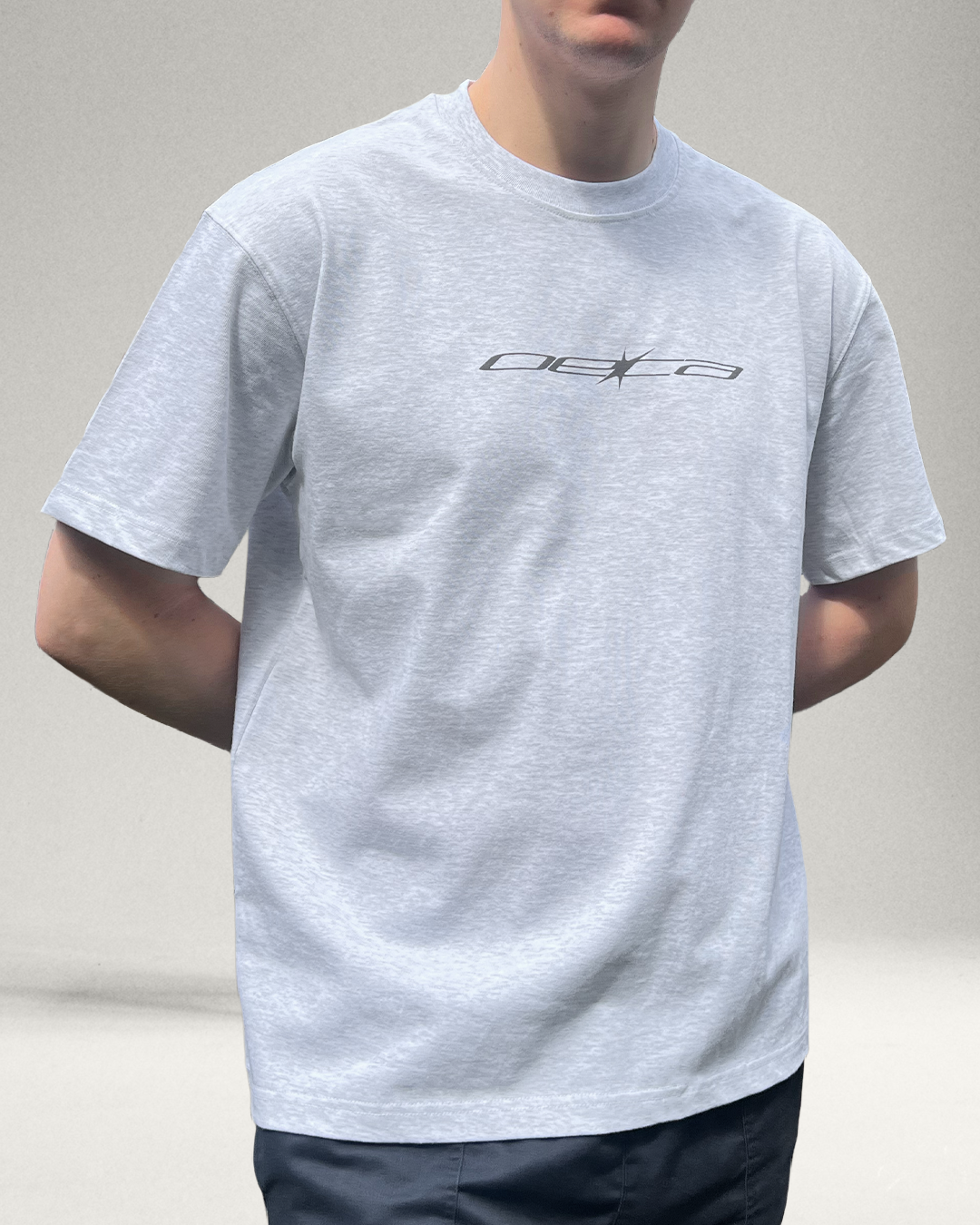 Person wearing a gray t-shirt with a logo on a plain background
