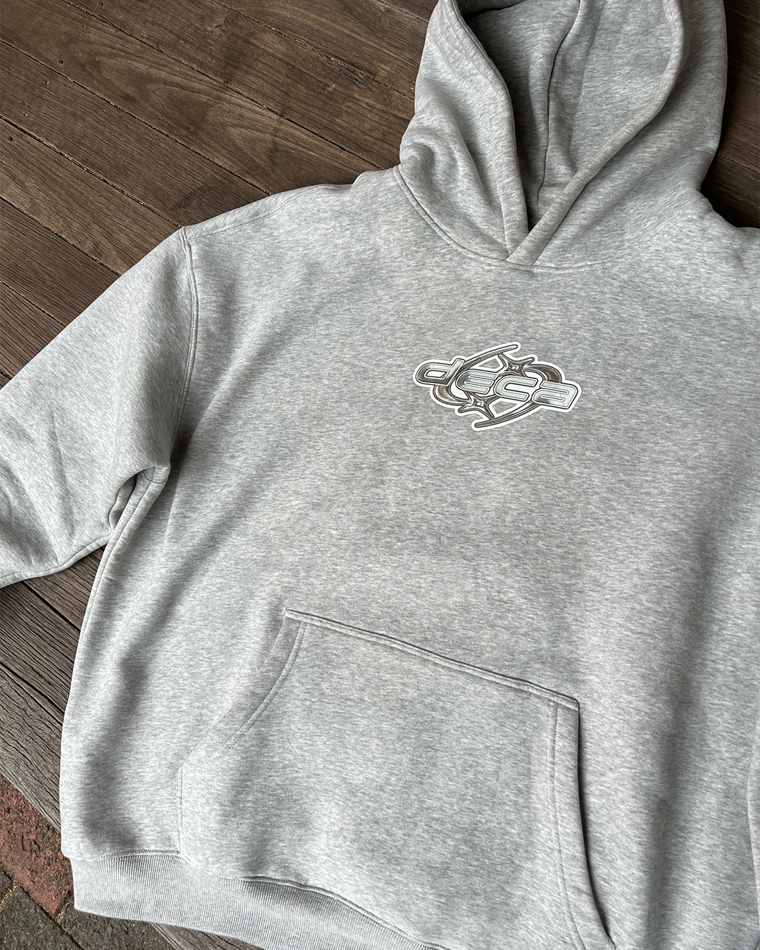 Gray hoodie with a abstract logo on the chest, placed on a wooden surface.