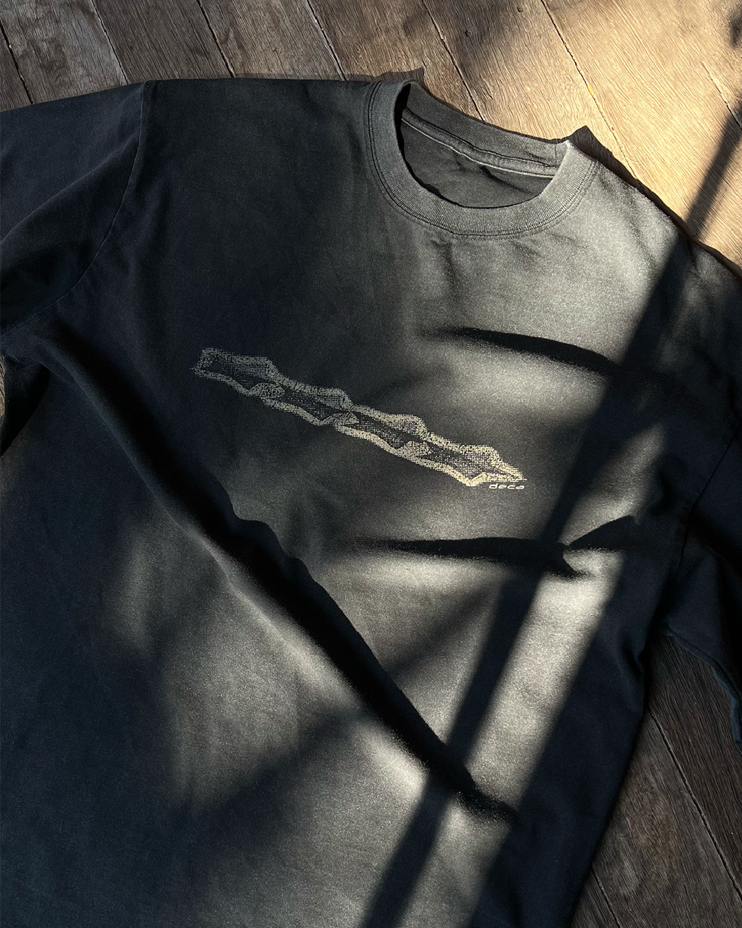 Black t-shirt with an abstract gold logo on a wooden floor